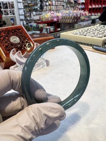 A person wearing gloves holding an object in front of a clock.