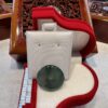 A white earring holder with a green glass bead in it.