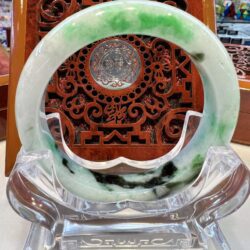 A green and white jade bracelet sitting on top of a glass display.