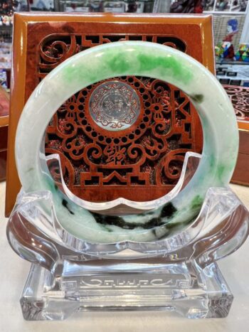 A green and white jade bracelet sitting on top of a glass display.