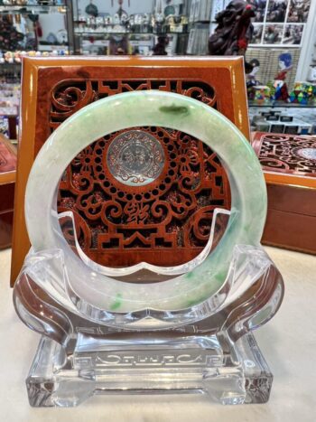 A green jade bracelet sitting on top of a clear glass plate.