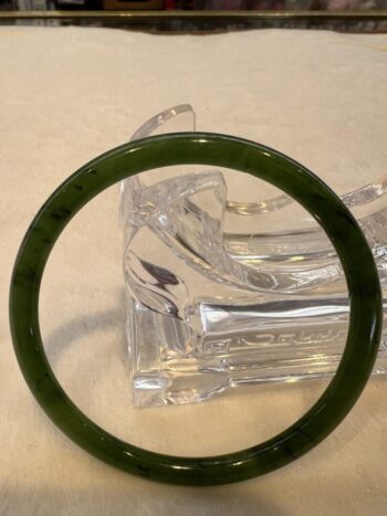 A green bangle sitting on top of a clear glass object.