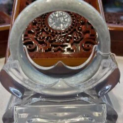 A glass clock with a round face and a wooden carved pattern.