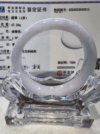 A white jade bangle sitting on top of a glass stand.