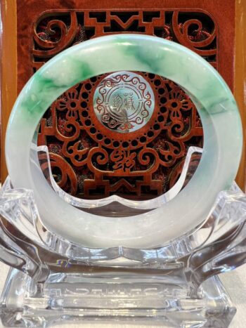 A green and white jade bangle sitting on top of a glass plate.