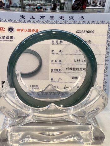 A green jade bangle is sitting on top of a clear glass.