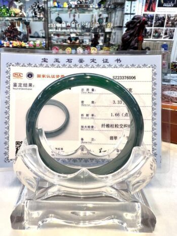 A green jade bangle is displayed in front of an asian certificate.