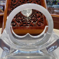 A clear plastic chair with a wooden carved table in the background.