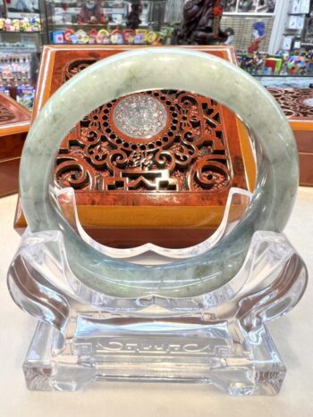 A large green jade bangle sitting on top of a clear glass stand.