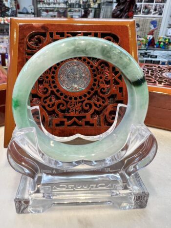 A green jade bracelet sitting on top of a clear glass display.