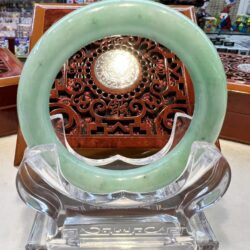 A green jade bangle sitting on top of a clear glass stand.