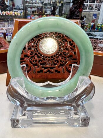 A green jade bangle sitting on top of a clear glass stand.