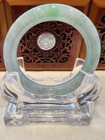 A green jade bangle sitting on top of a clear glass stand.