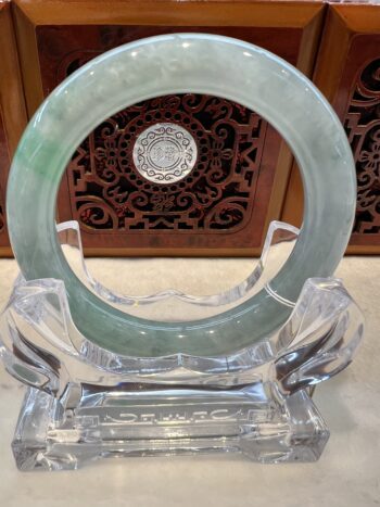 A green jade bracelet sitting on top of a clear glass stand.