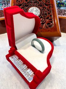 A red velvet ring box with a green bracelet inside of it.