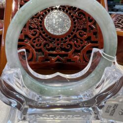 A round green jade ring sitting on top of a glass stand.