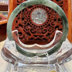 A green and white jade circular ring sitting on top of a clear glass stand.