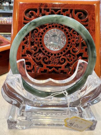 A green and white jade circular ring sitting on top of a clear glass stand.