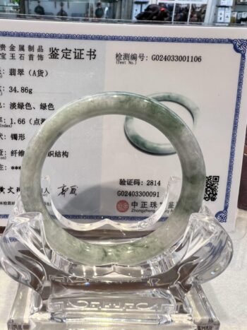 A green jade bracelet is displayed in front of an official certificate.