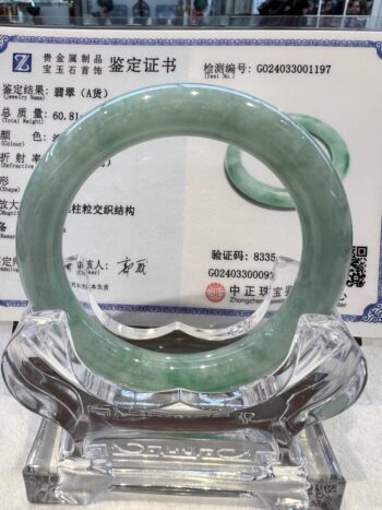 A green jade bangle is sitting on top of a glass display.