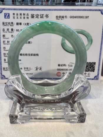 A green jade bangle is sitting on top of a glass display.