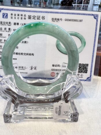 A green jade bangle is displayed in front of an official certificate.