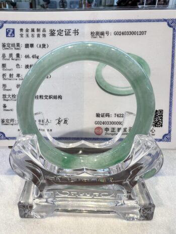 A green jade bangle is sitting on top of a glass display.