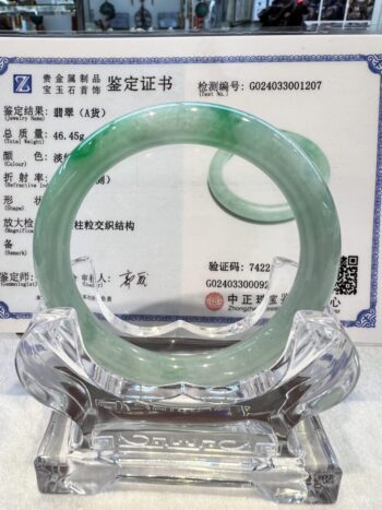 A green jade bangle is sitting on top of a glass display.