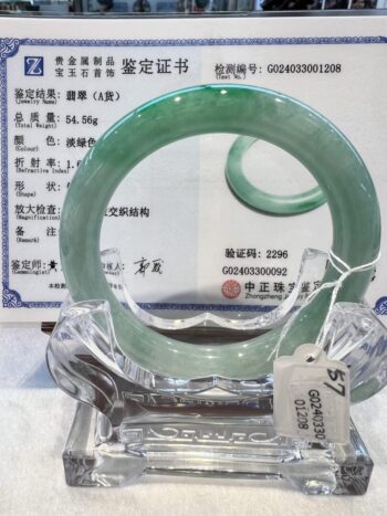 A green jade bangle is sitting on top of a clear glass.