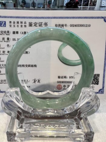 A green jade bangle is sitting on top of a glass table.