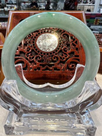 A green jade bangle sitting on top of a clear glass.