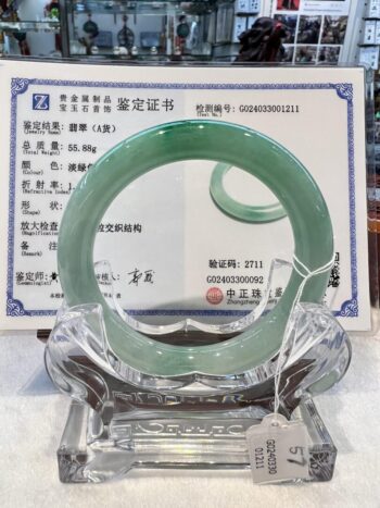 A green jade bangle is displayed in front of an official certificate.