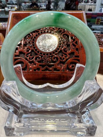 A green jade bangle sitting on top of a clear glass table.