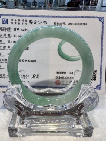 A green jade bangle is sitting on top of a glass display.