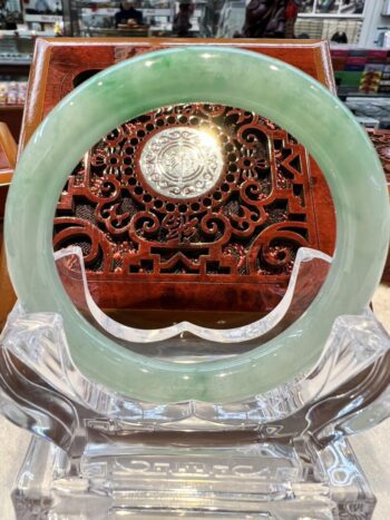 A green jade bangle sitting on top of a clear glass table.