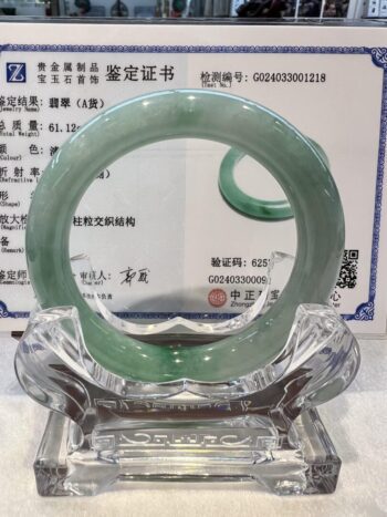 A green jade bangle is sitting on top of a glass stand.