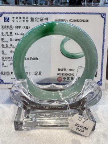 A green jade bangle is sitting on top of a clear glass display.