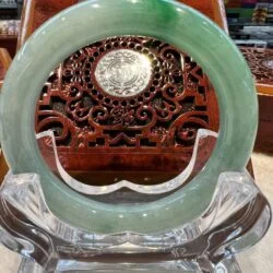 A green jade circular plaque sitting on top of a wooden stand.