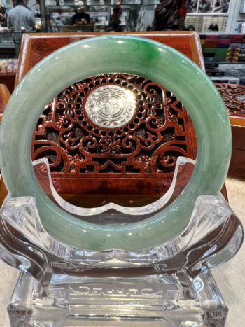 A green jade circular plaque sitting on top of a wooden stand.