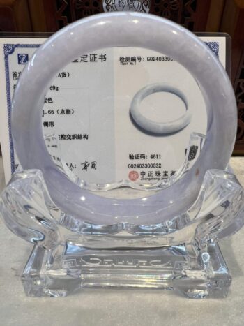 A white jade bangle sitting on top of a clear glass stand.