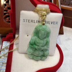 A green jade buddha necklace sitting on top of a red box.