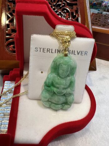 A green jade buddha necklace sitting on top of a red box.