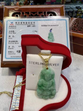 A green jade buddha pendant sitting in a red box.