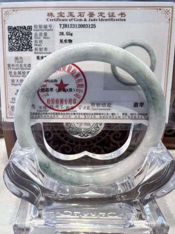 A white jade bangle sitting on top of a clear glass display.