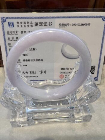 A white jade bangle sitting on top of a clear glass display.