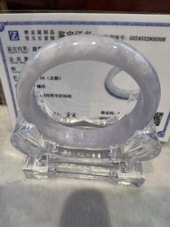 A white jade bangle sitting on top of a clear glass stand.