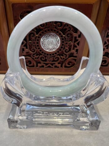 A white jade bangle sitting on top of a clear glass stand.