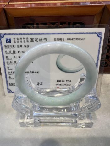 A white jade bangle sitting on top of a glass display.