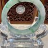 A green and white jade bracelet sitting on top of a clear glass stand.
