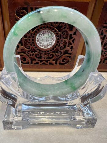 A green and white jade bracelet sitting on top of a clear glass stand.